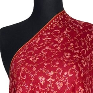 A close-up shot of a red semi-pashmina shawl draped on a black mannequin, featuring intricate light-colored floral and swirling embroidery patterns across the fabric.