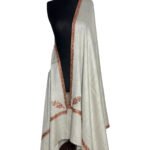 Elegant off-white semi-pashmina shawl with delicate burnt orange or rust-colored embroidery along the borders and corners, draped on a black mannequin.